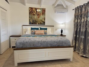 Een netjes ingerichte slaapkamer met een bed, een nachtkastje met een lamp, een schilderij boven het bed en een raam met gordijnen.