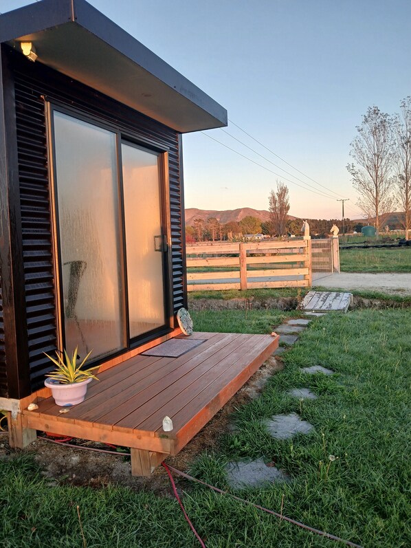 A modern house with a wooden deck, a sliding glass door, and a small garden area with a potted plant.