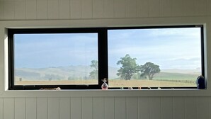 A room with a large window overlooking a rural landscape with hills and trees.