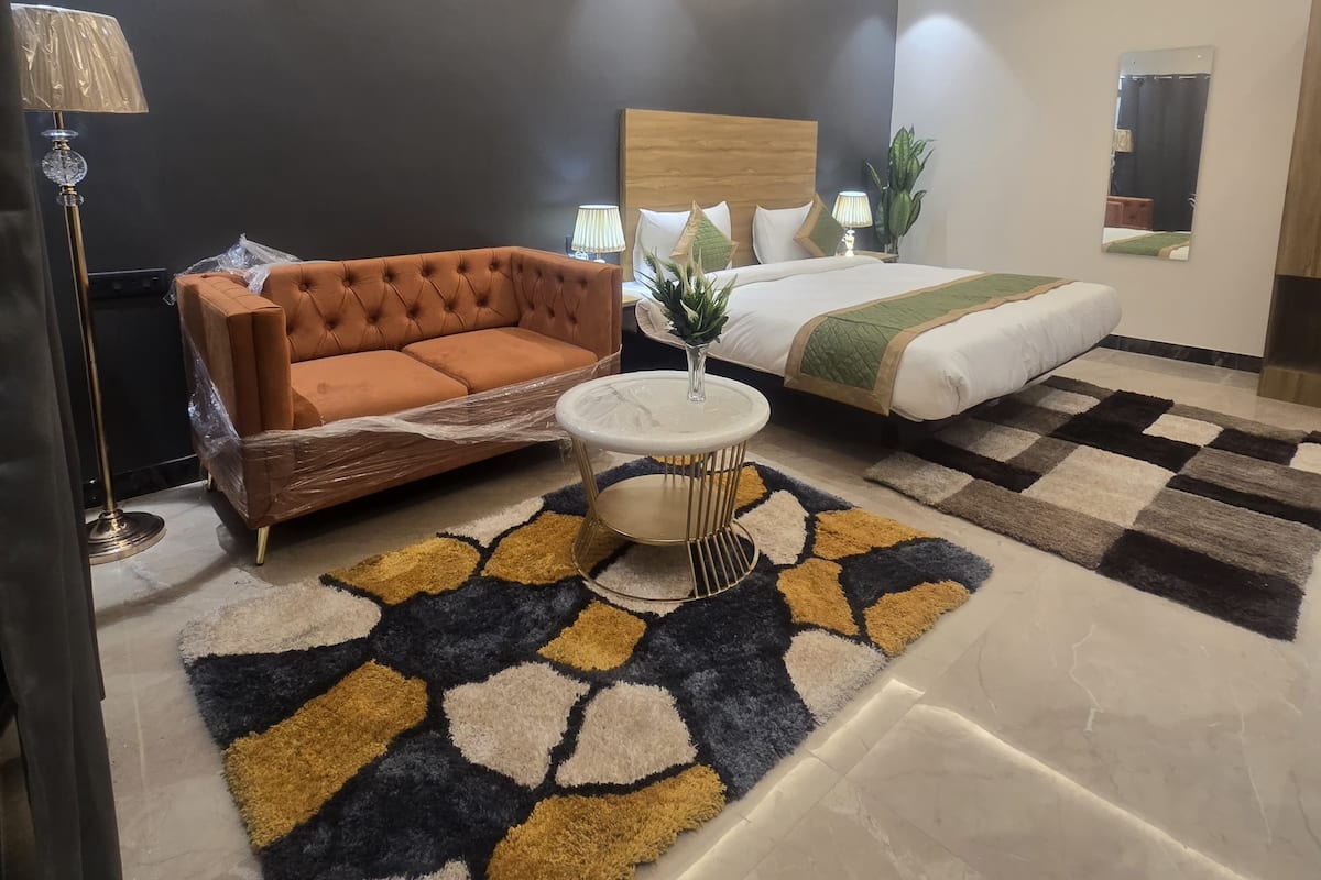 Une chambre d’hôtel moderne avec un canapé, un lit, une table basse ronde et un tapis à motifs.