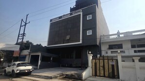 A modern building with a large glass facade, a gated entrance, and a white car parked in front. - Hotel Golden Tulip'z (Gorakhpur)