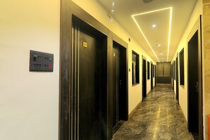 Un couloir d’hôtel avec les portes numérotées 202 et 203, un panneau de commande et un sol en marbre.