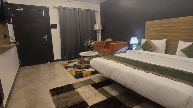 A modern hotel room with a large bed, a small round table, a lamp, and a dark curtain. - Hotel Golden Tulip'z (Gorakhpur)