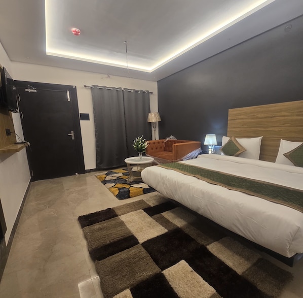 A modern hotel room with a large bed, a small round table, a lamp, and a dark curtain.