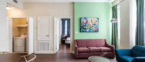 A living room with a red sofa, a blue armchair, a coffee table, and a painting on the wall.
