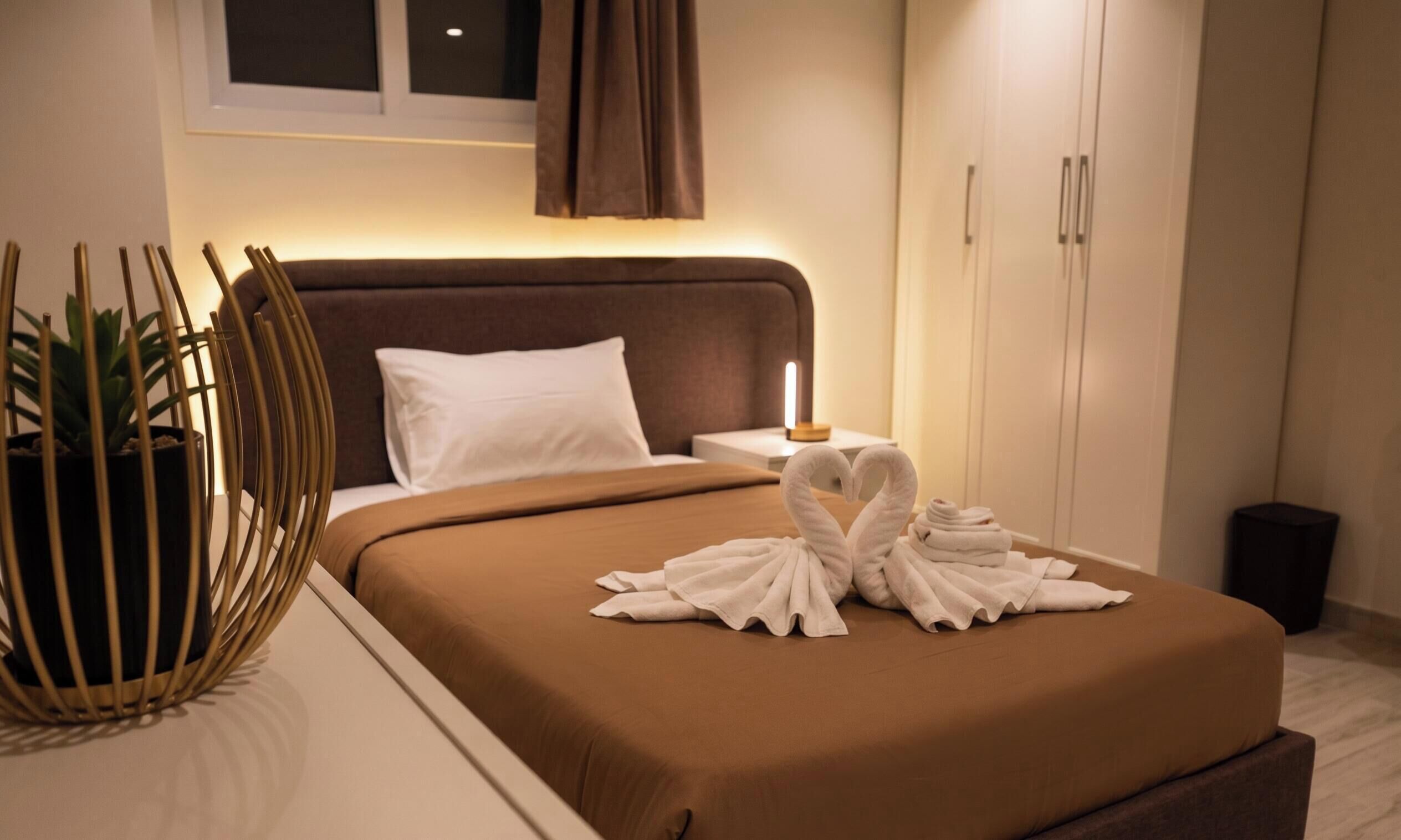 Habitación de hotel con cama, mesita de noche con lámpara, planta en maceta y armario.
