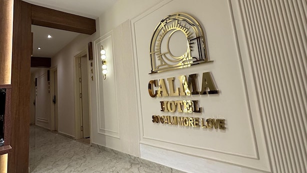 Un pasillo con piso de mármol, un cartel en la pared que dice "CALMA HOTEL" y un arco decorativo.