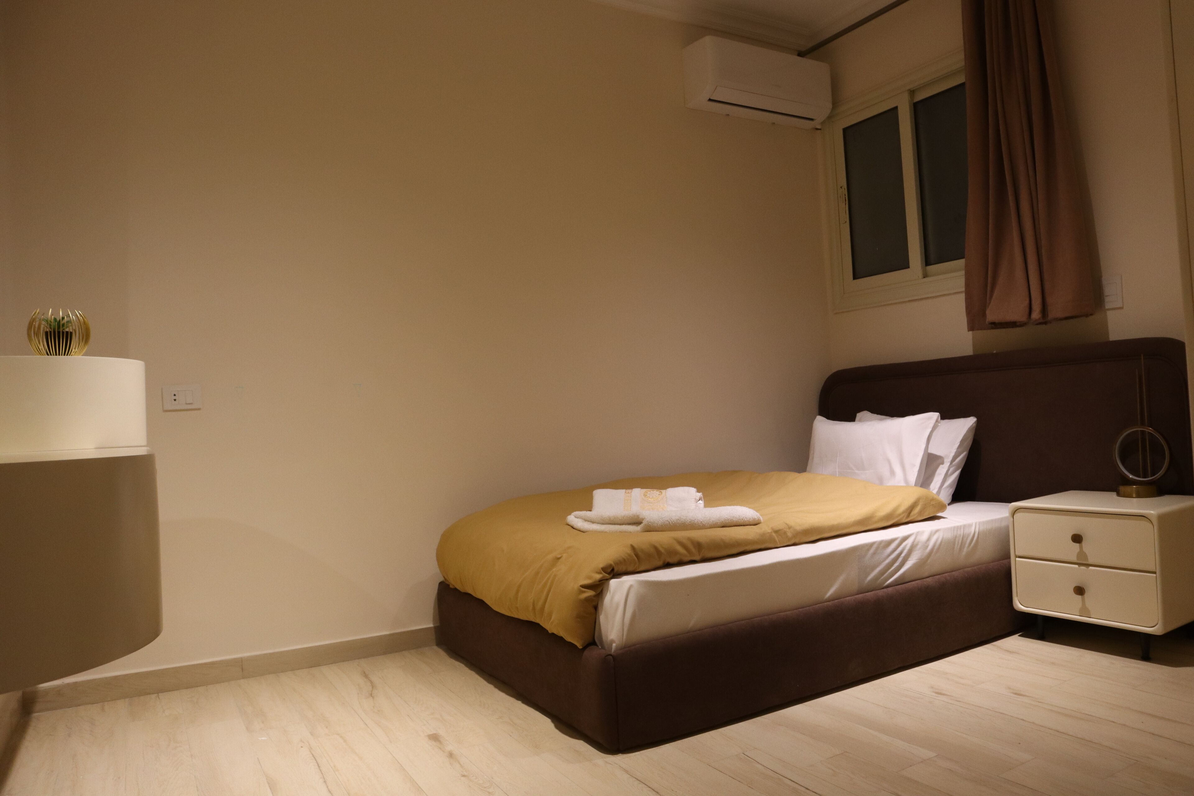 A bedroom with a bed, bedside table, and an air conditioning unit.