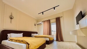 Habitación de hotel con dos camas, televisor de pantalla plana, unidad de aire acondicionado y ventana con cortinas.