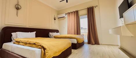 A hotel room with two beds, a flat-screen TV, an air conditioning unit, and a window with curtains.