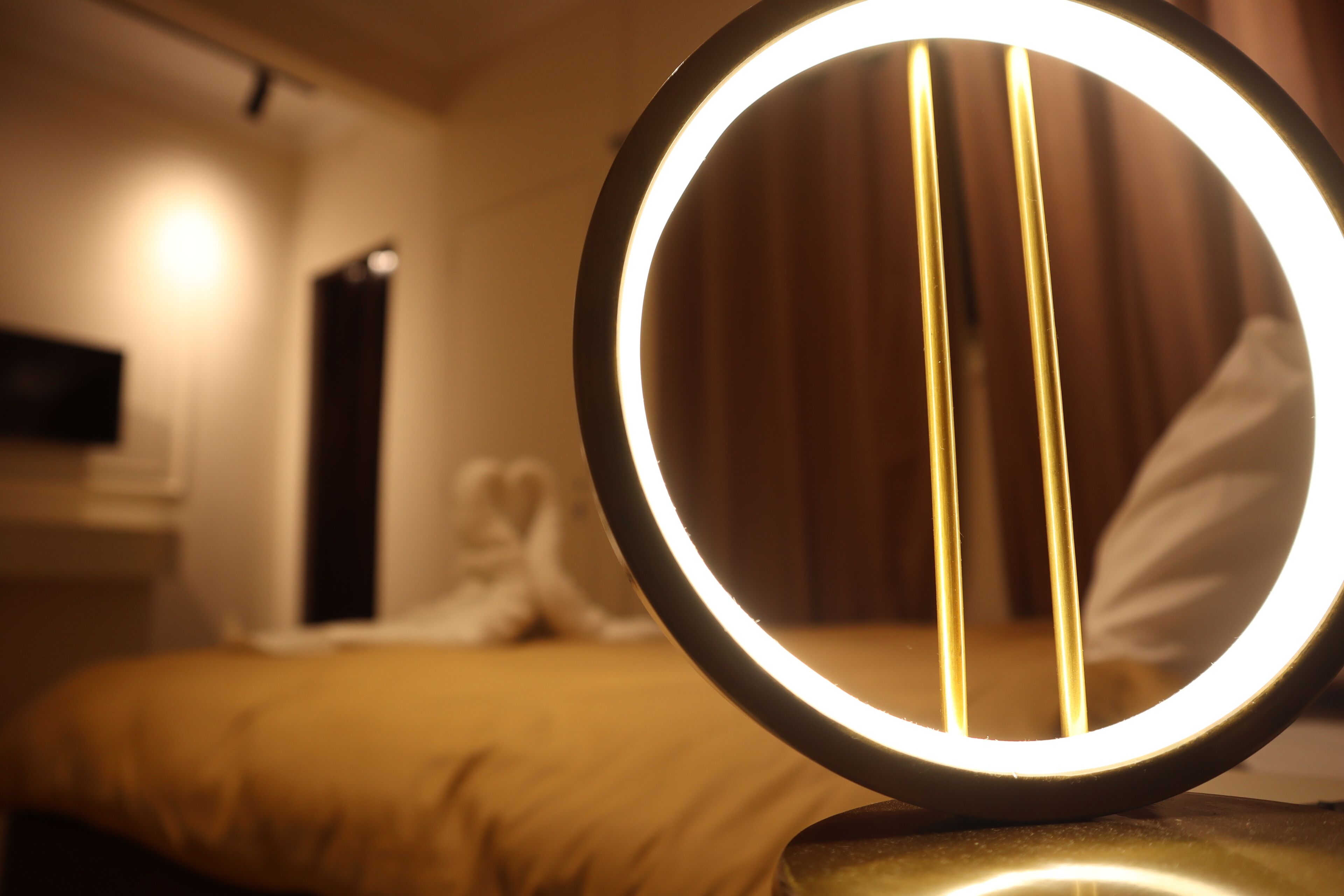 A circular mirror with a light ring, placed on a surface in a room with a bed and a nightstand.