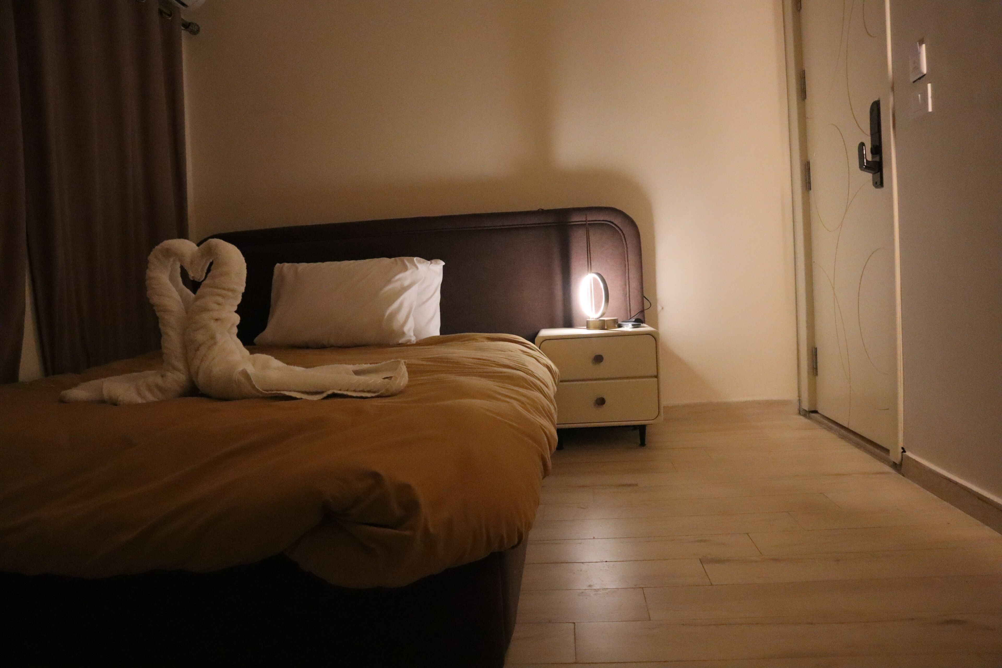 A hotel room with a bed, a nightstand, a lamp, and a door.
