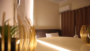 Una habitación de hotel con cama, cabecera, cortina y aire acondicionado instalado en la pared.