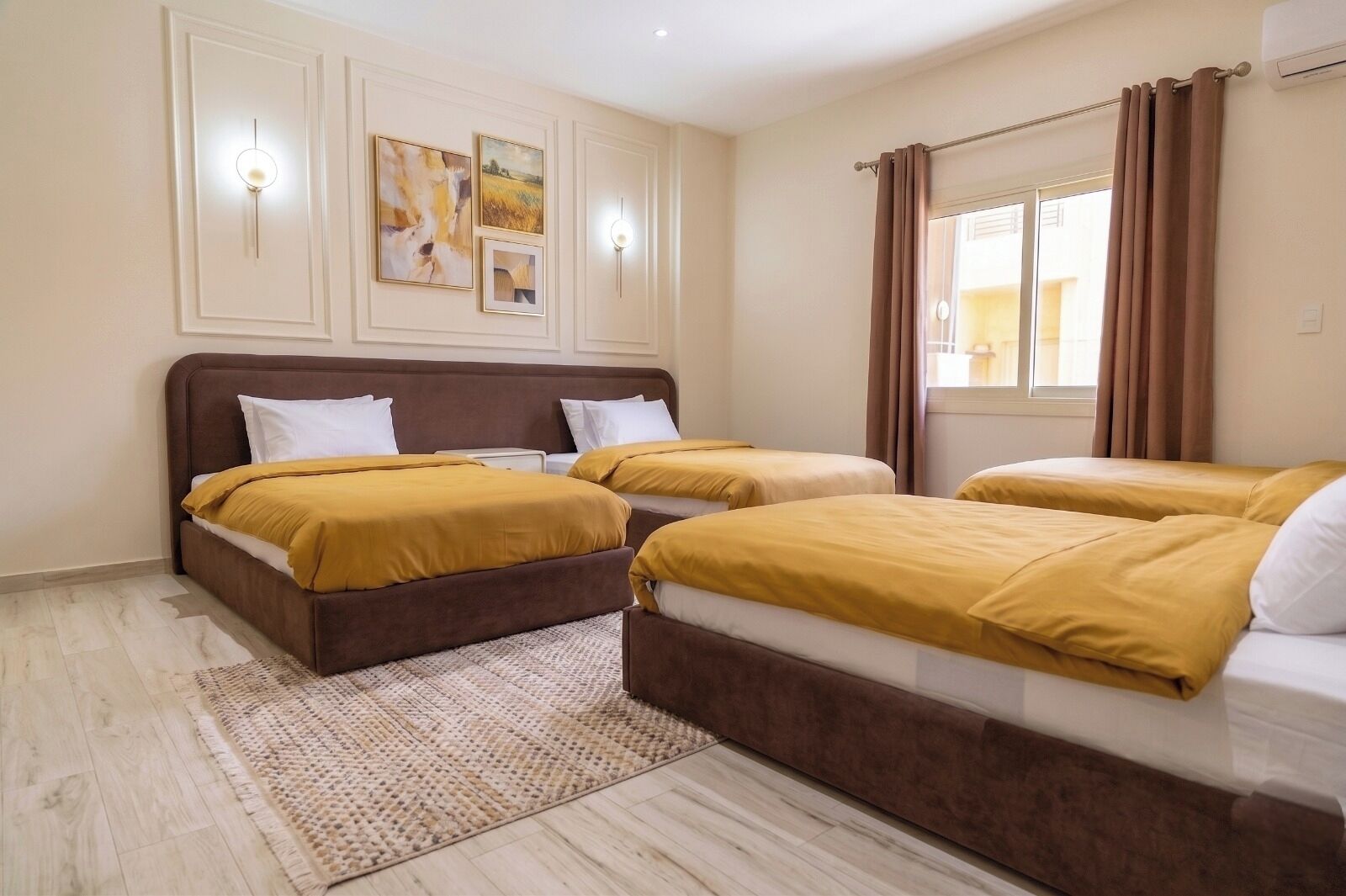 A hotel room with two beds, a large window with curtains, and wall-mounted lighting.