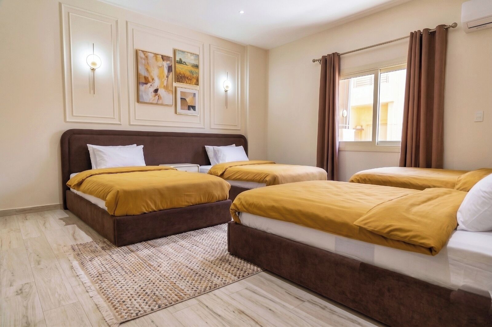 A hotel room with two beds, a large window with curtains, and wall-mounted artwork.