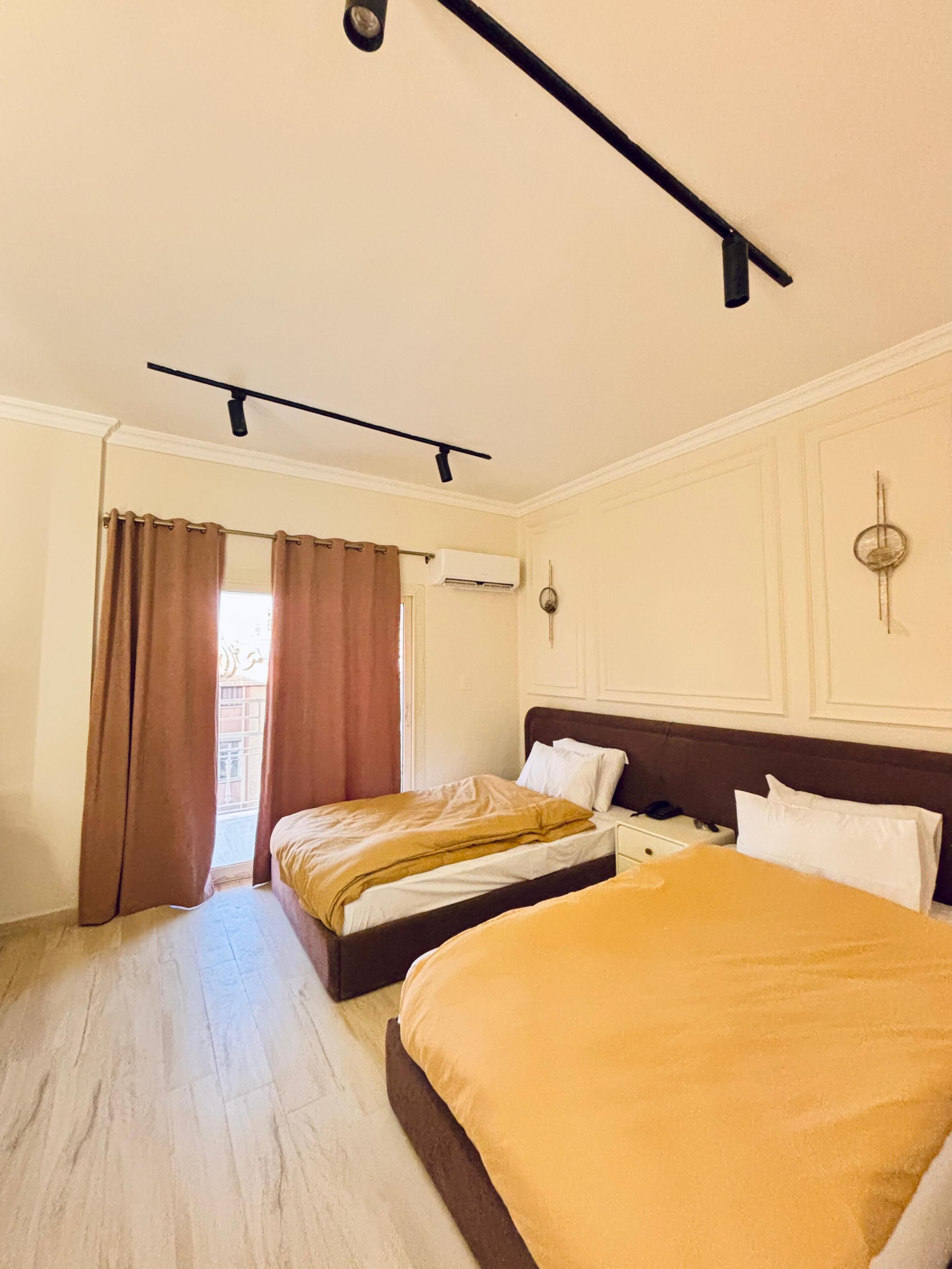 A hotel room with two beds, a ceiling fan, an air conditioning unit, and a view of the outside balcony.