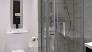 Een moderne badkamer met een glazen douchecabine, een toilet en een klein raam met een bloevas.