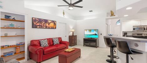 A modern living room with a red sofa, a coffee table, a TV, and a kitchen area with a bar.