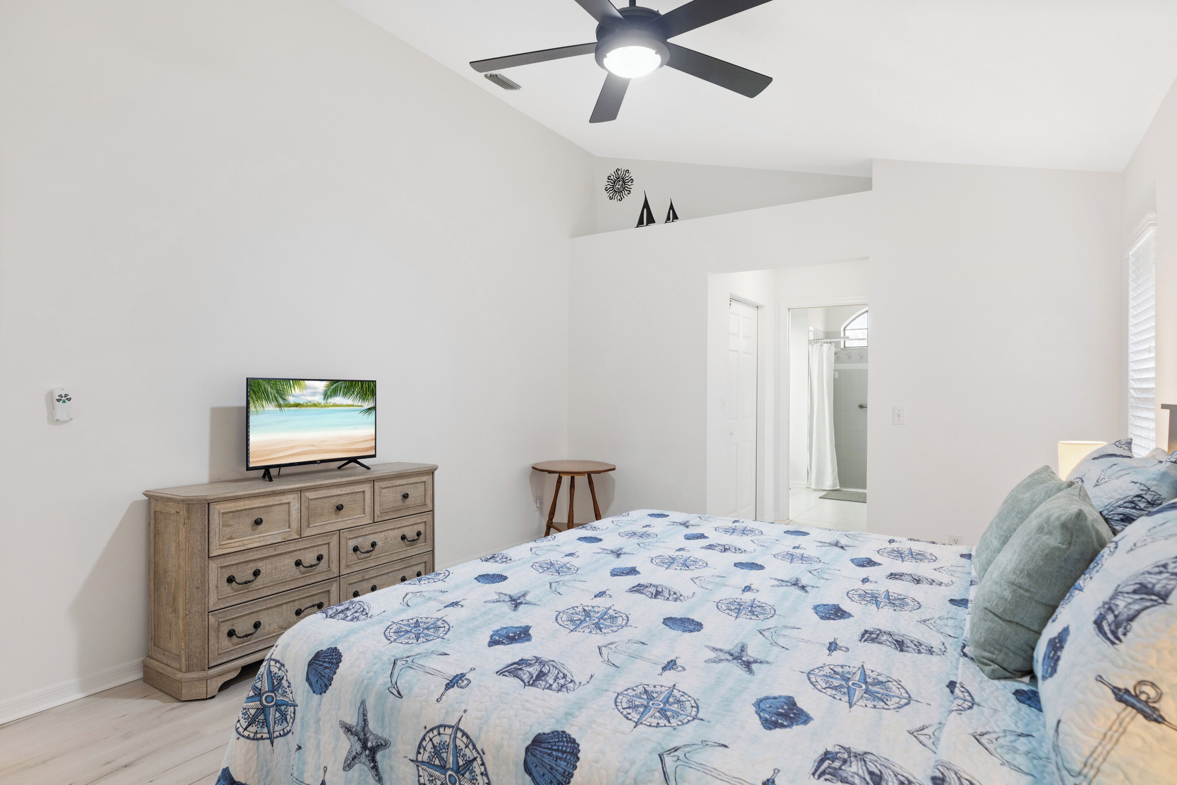 A bedroom with a bed, a dresser, a television, and a ceiling fan.