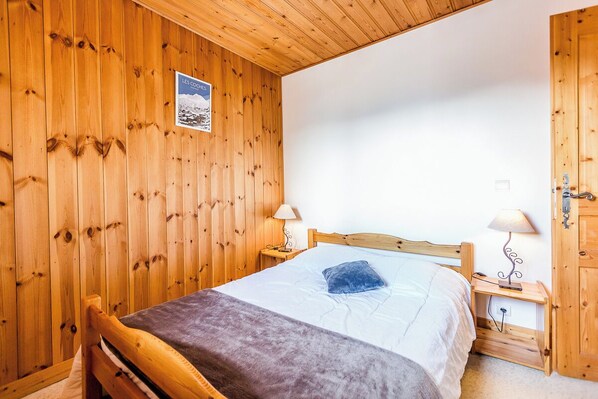 Une chambre à coucher aux murs lambrissés, avec un lit, deux tables de chevet dotées de lampes et une porte.