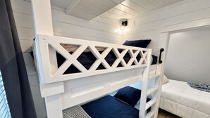 Una cama litera con estructura blanca, una cama inferior con colchón azul y una cama individual con colchón blanco.