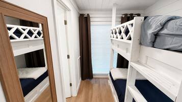 Ein Zimmer mit Etagenbetten, Holzboden und einem Fenster mit Jalousien.