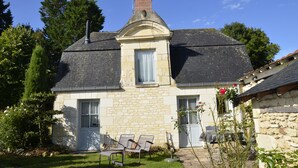 A stone house with a chimney, a door, and a window. There are two chairs outside. - Le Petit Pavillon, located in the heart of the Anjou vineyards between Angers and Saumur (Tuffalun)