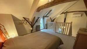 A bedroom with a large bed, wooden beams, a balcony, and an air conditioning unit. - Le Petit Pavillon, located in the heart of the Anjou vineyards between Angers and Saumur (Tuffalun)