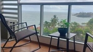 Een balkon met uitzicht op zee, een stoel, een tafeltje en een plant in een pot.