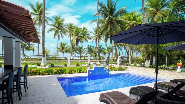 Une piscine entourée de palmiers et d’un jardin bien entretenu, avec des chaises longues et des parasols à disposition.