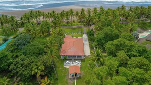 Un complexe hôtelier tropical avec vue sur la plage, des palmiers et une maison avec un toit rouge.
