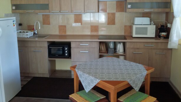 A compact kitchen with wooden cabinets, a microwave, a toaster, and a small table with a tablecloth. - Comfortable vacation home in a quiet area close to Lake Balaton (Szántód)