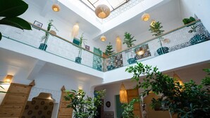 A multi-level atrium with a glass ceiling, wooden railings, and hanging lights. - Riad Lkhlil (Marrakech)