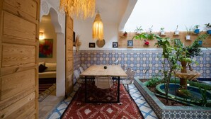 A cozy indoor space with a wooden wall, a tiled wall with a blue and white pattern, a hanging light fixture, a table with chairs, and a small fountain. - Riad Lkhlil (Marrakech)