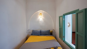 A bedroom with a bed, a wall-mounted light, and a window with green shutters. - Riad Lkhlil (Marrakech)