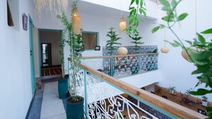 A spacious indoor area with a wooden staircase, potted plants, hanging lights, and a decorative railing. - Riad Lkhlil (Marrakech)