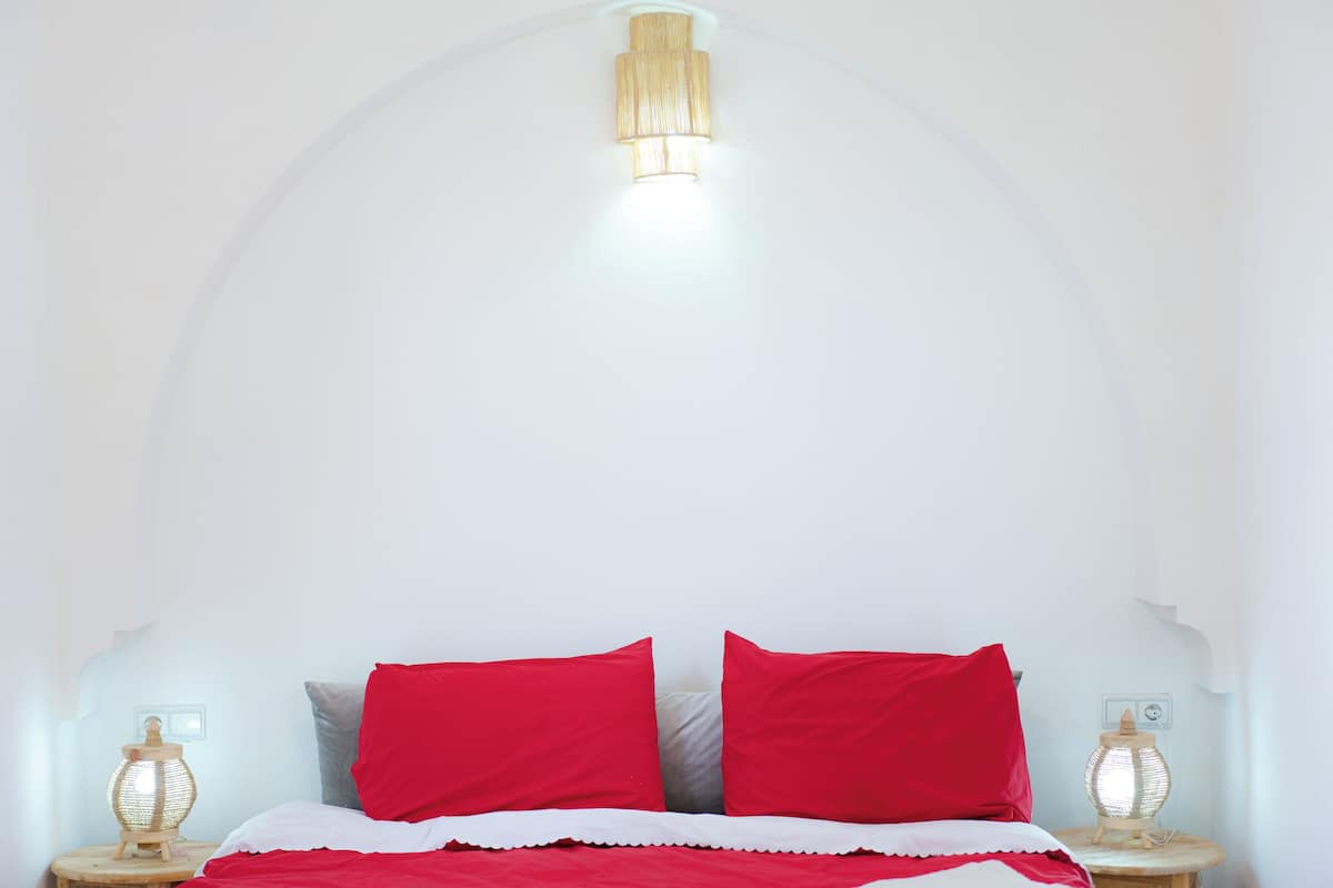 Une chambre à coucher avec un plafond blanc, un lit avec une literie rouge et blanche, et deux lampes de chevet.
