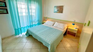 Un dormitorio con cama, mesita de noche, lámpara, ventana con cortinas y un cuadro en la pared.