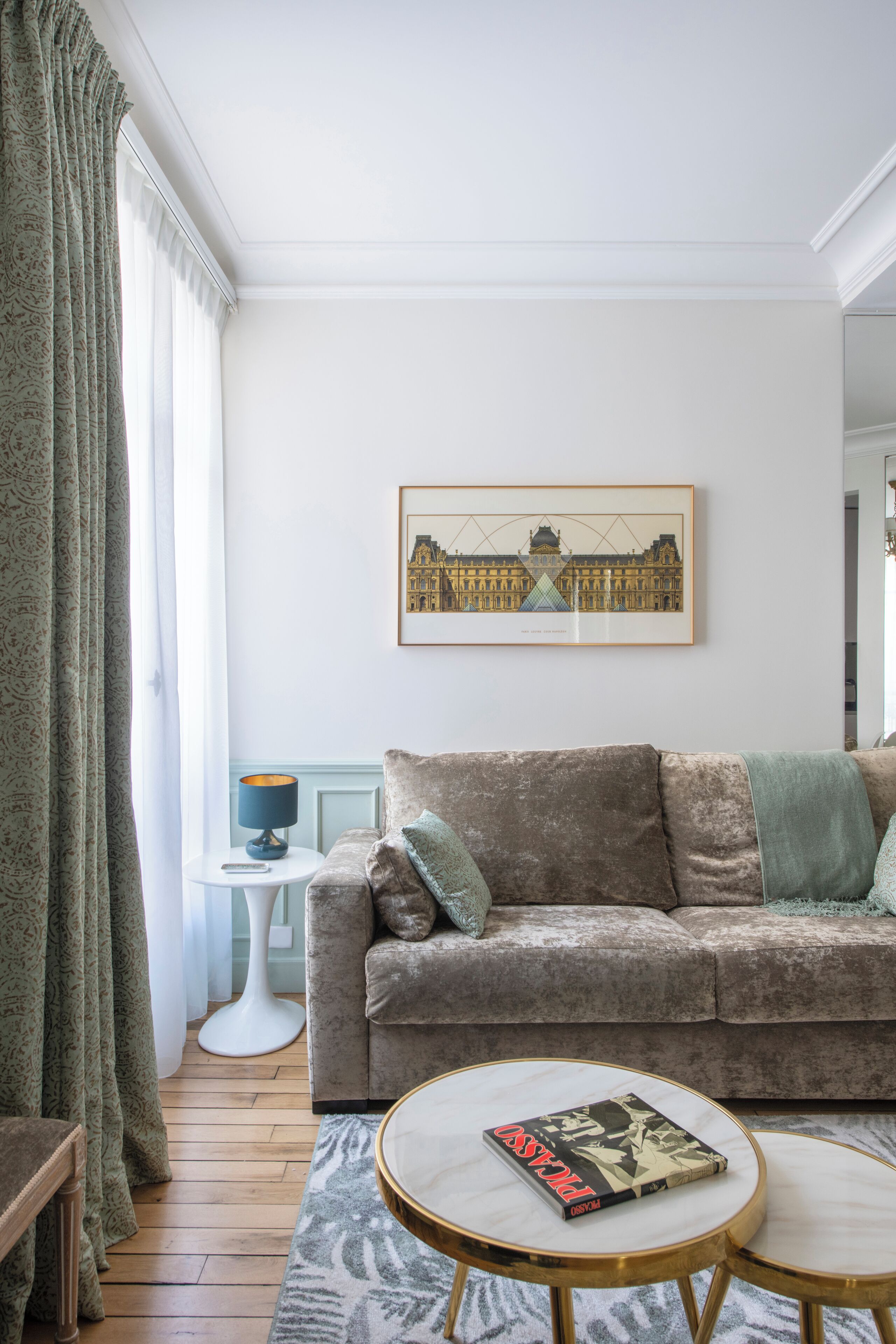 A living room with a sofa, two round tables, a framed picture on the wall, and a patterned rug.