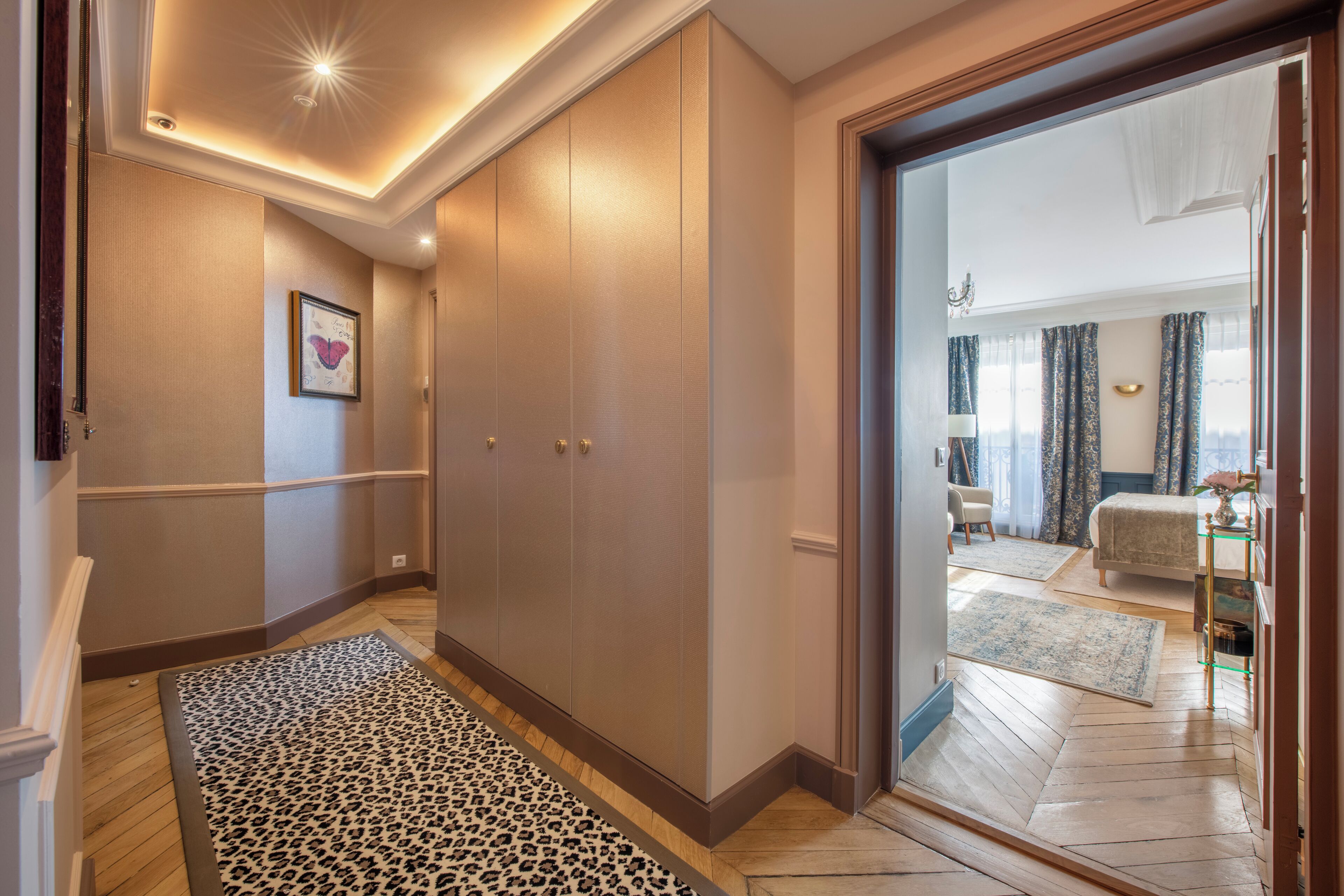 Ein Flur mit einem Leopardenmuster-Teppich, einem großen Kleiderschrank und Blick in ein Schlafzimmer mit Bett und Nachttisch.