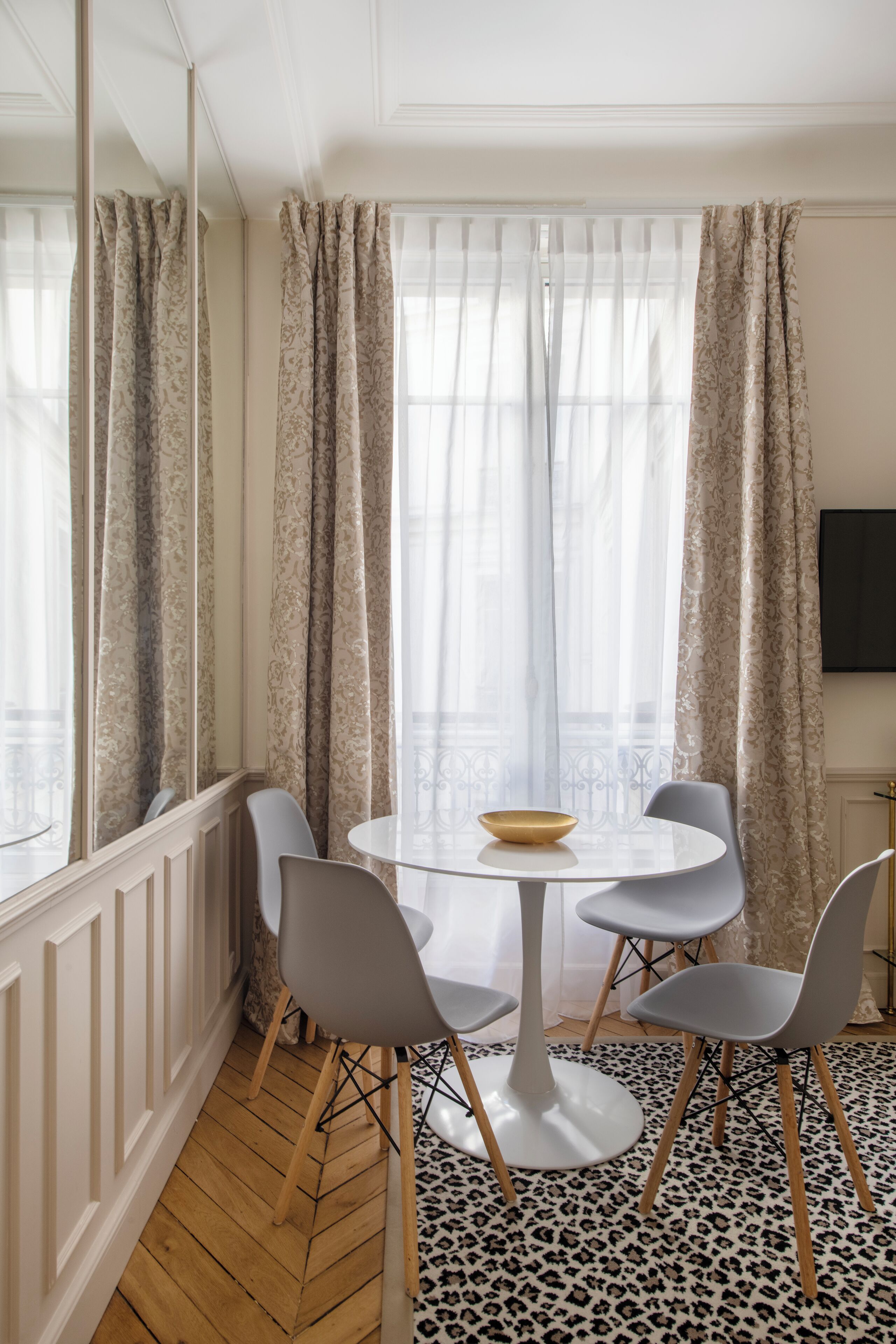 A dining area with a round table, four chairs, a bowl, and a leopard print rug.