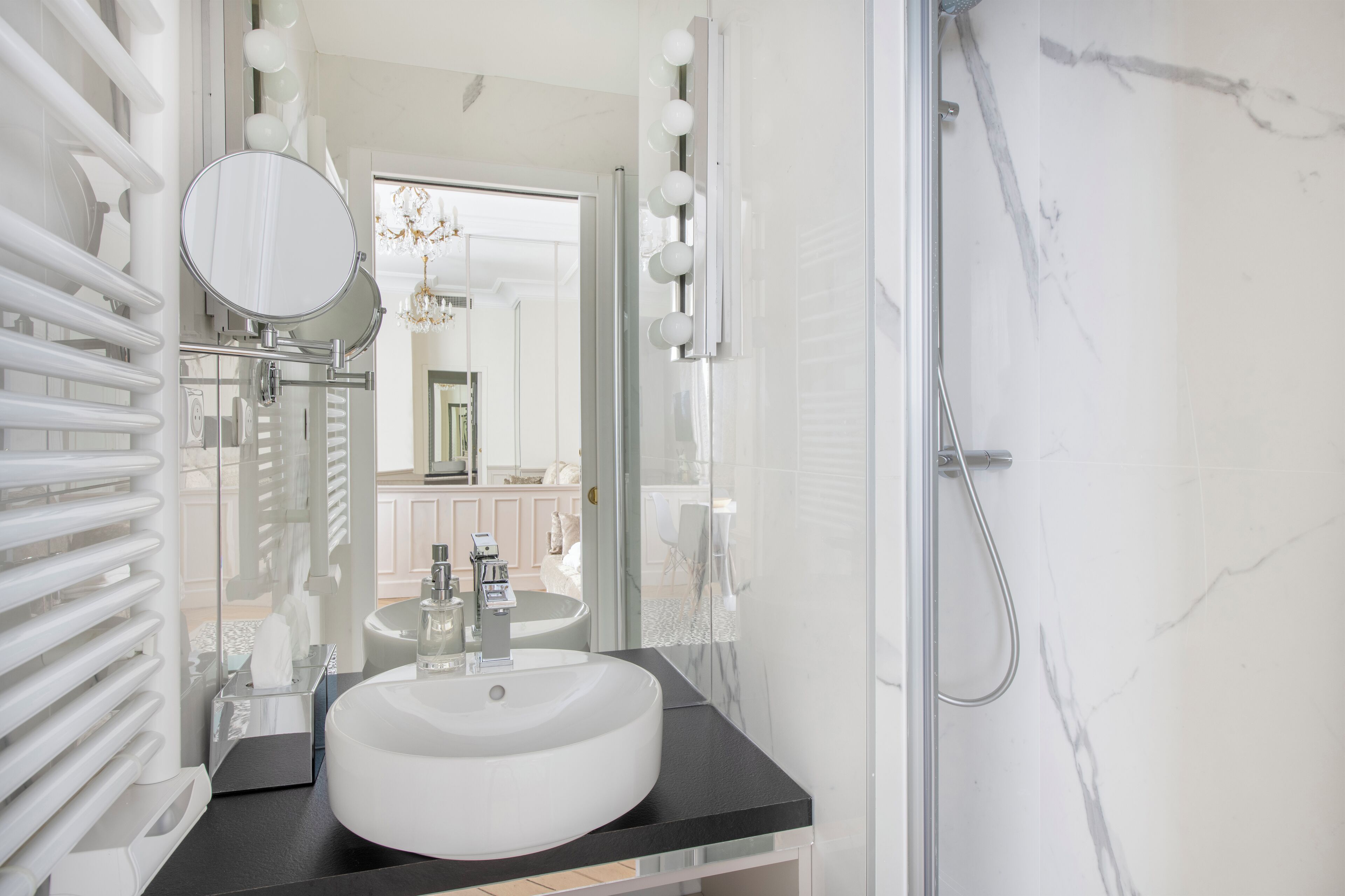 Un baño moderno con un lavamanos blanco, encimera negra y cabina de ducha de vidrio.
