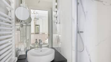 Un baño moderno con un lavamanos blanco, encimera negra y cabina de ducha de vidrio.