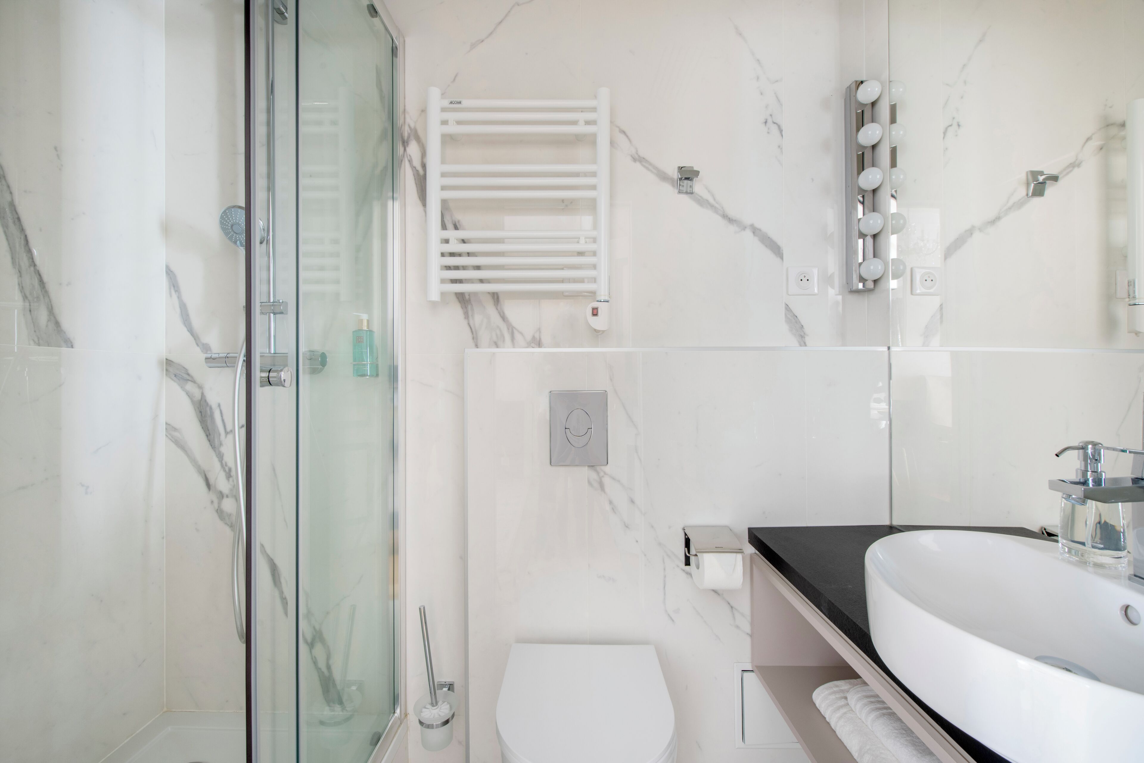 Een moderne badkamer met een douche met glazen wand, een wit toilet, een wastafel met een zwart aanrechtblad en een handdoekrek.