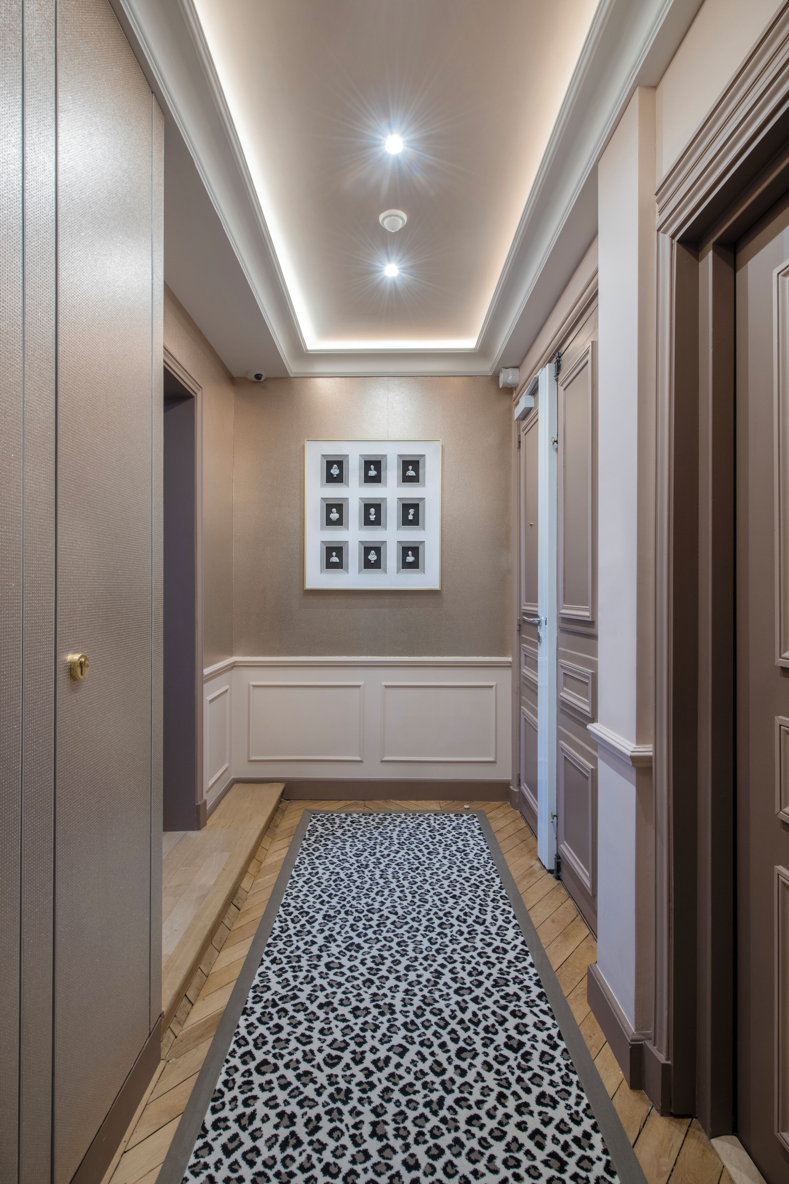 Um corredor com tapete estampado, quadros nas paredes e luminária no teto.