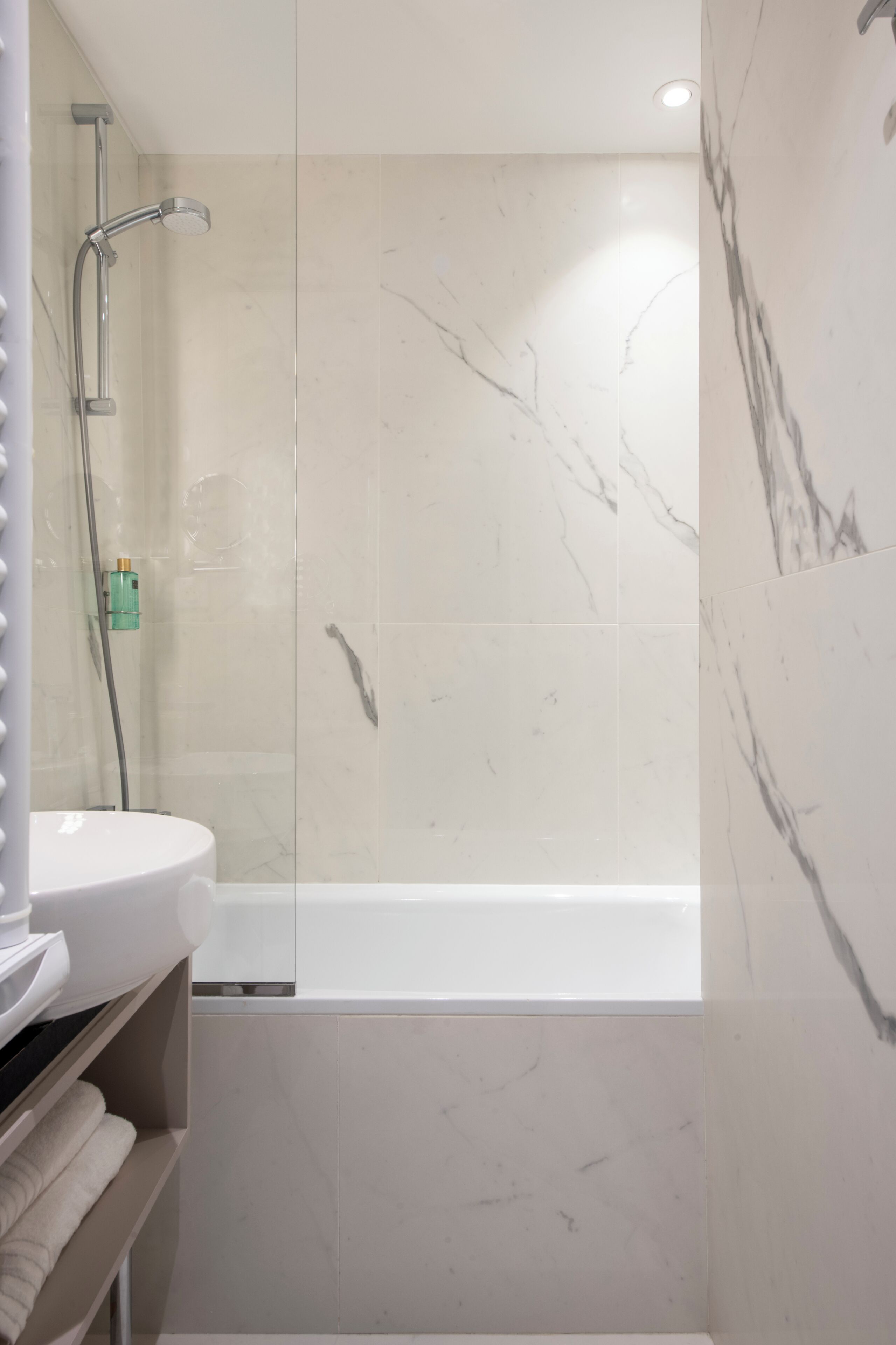 A bathroom with a glass-enclosed shower, a white sink, and marble tiles.
