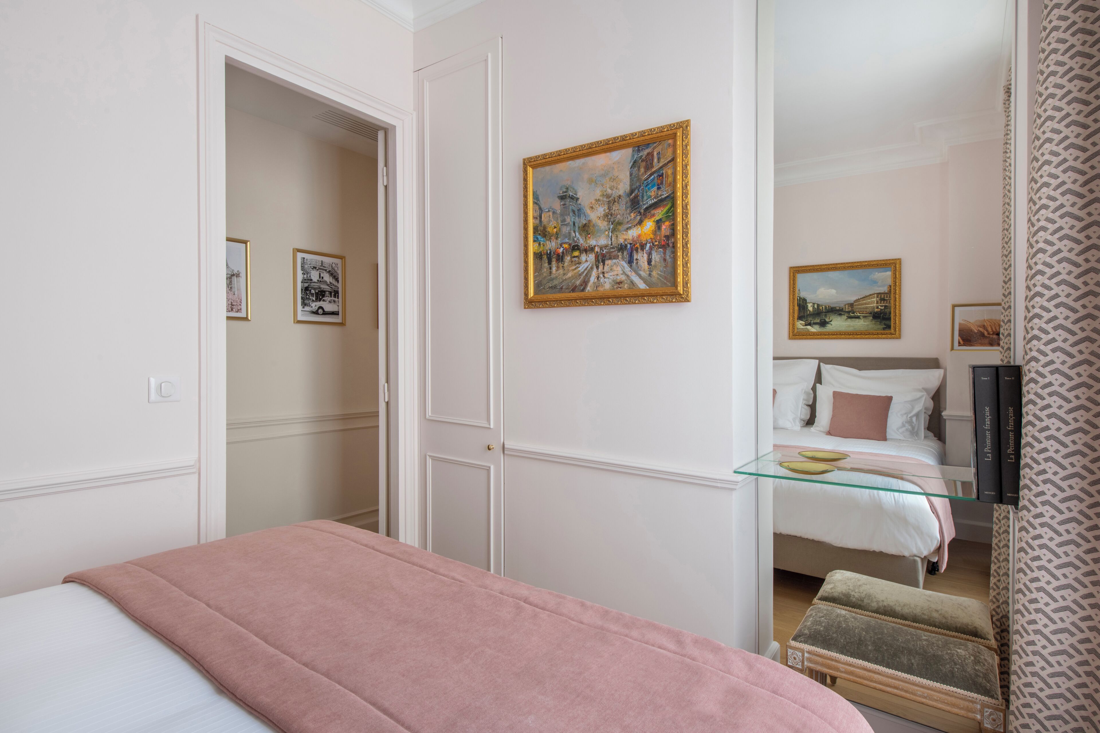 A hotel room with a bed, a glass table, a chair, and two paintings on the wall.