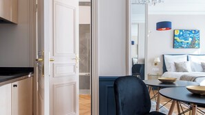 Una habitación de hotel moderna con zona de comedor, una araña y un cuadro en la pared.