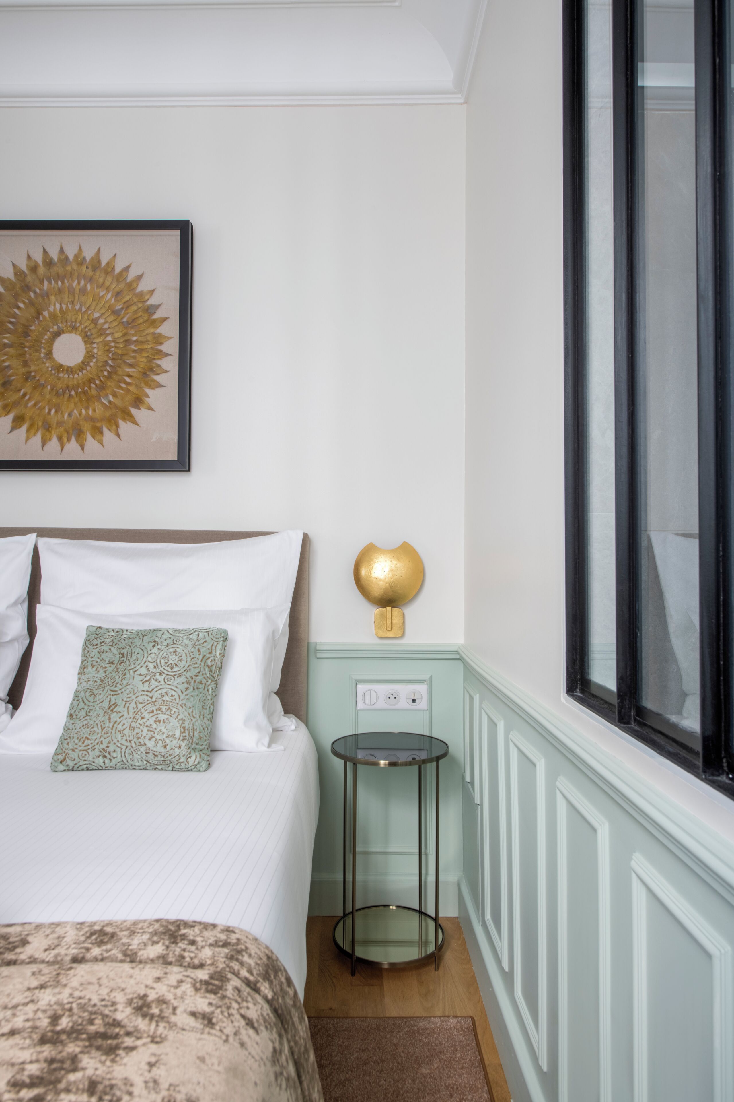Een keurig opgemaakt slaapkamer met een bed, kussens, een nachtkastje, een lamp en een raam.