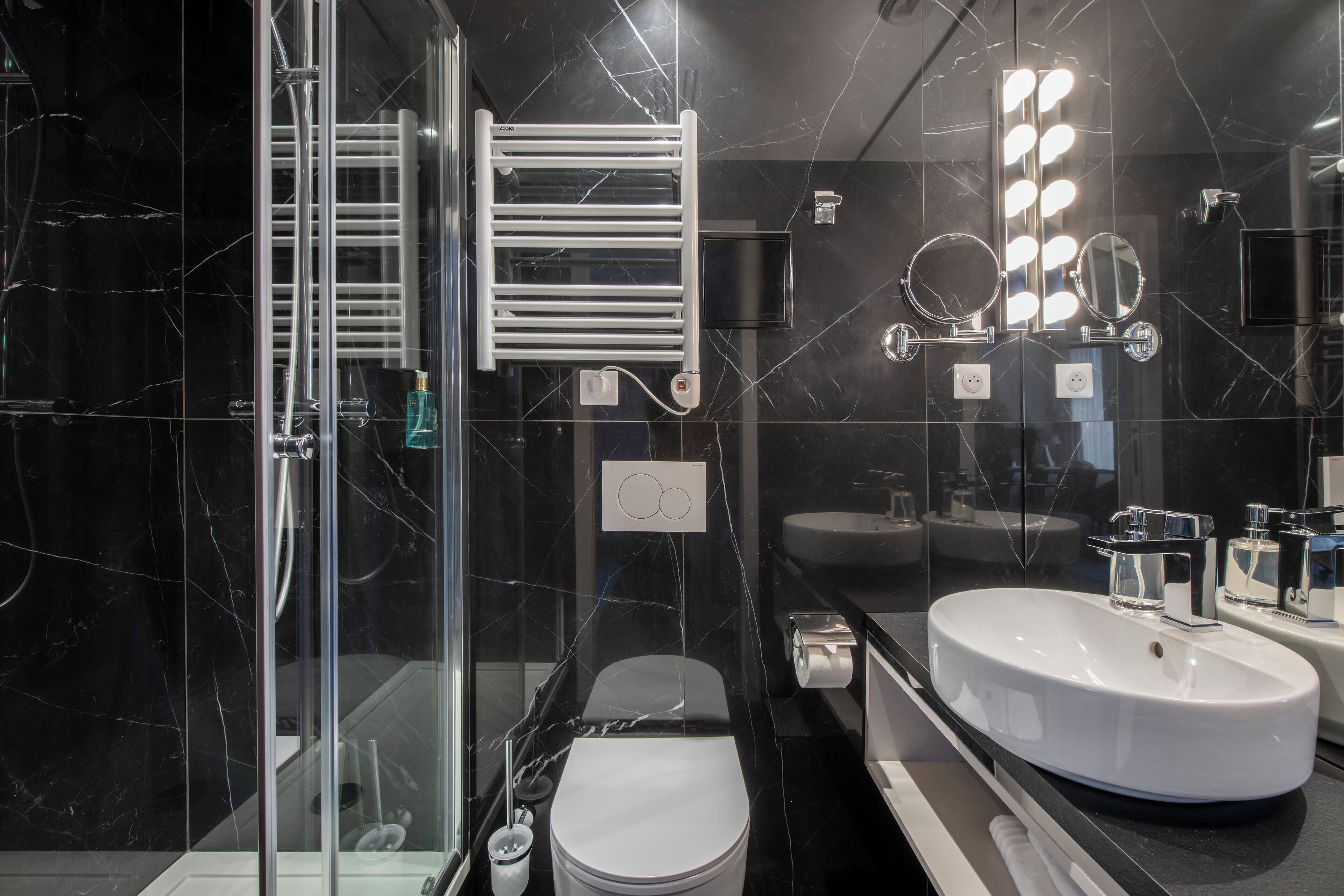 A modern bathroom with a glass-enclosed shower, a white toilet, a vanity with a large sink, and a mirror with lights.